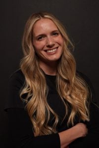 A smiling woman with long blonde hair wearing a black shirt.