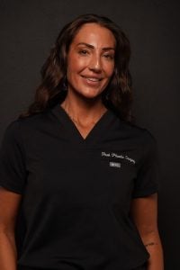 A woman in a black scrub top with “Peak Plastic Surgery” embroidered on the chest.