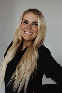 A smiling woman with long blonde hair wearing a black top.